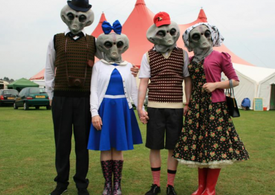4 people wearing alien masks are stood with their arms around, holding hands.