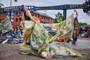 An outdoor performance - A woman is wrapped in a piece of dirty netting, leaning back as if trying to breathe.